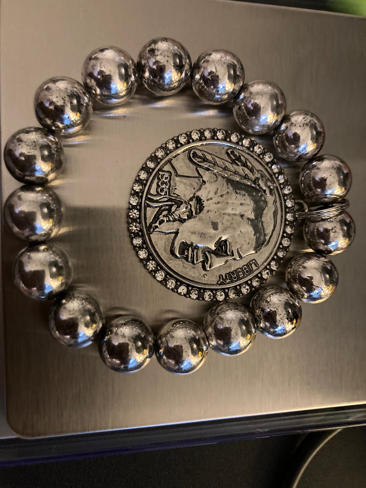 Bracelet with metallic beads and a coin with gems design on a reflective surface.