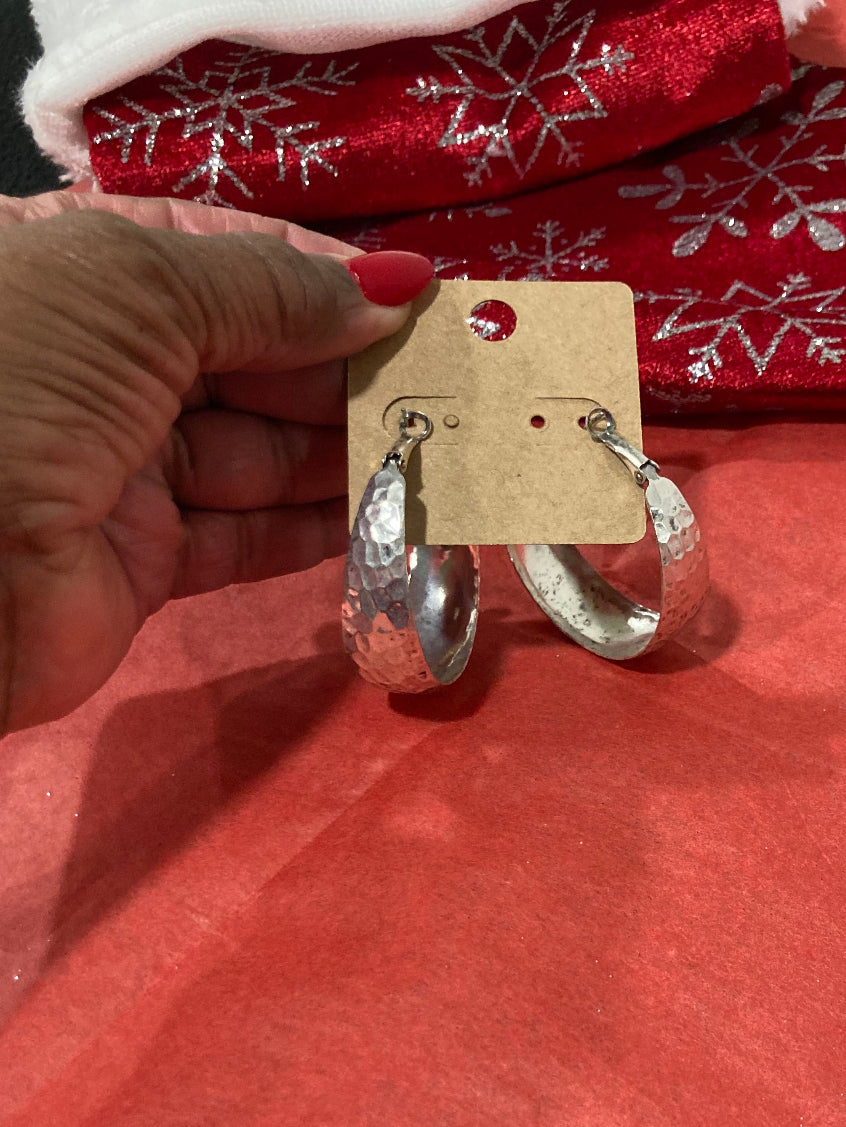 Hand holding a pair of small silver earrings on a tag and red fabric background