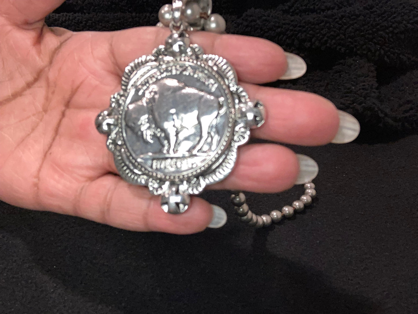 Silver plated Bison pendant held in a hand against a dark background