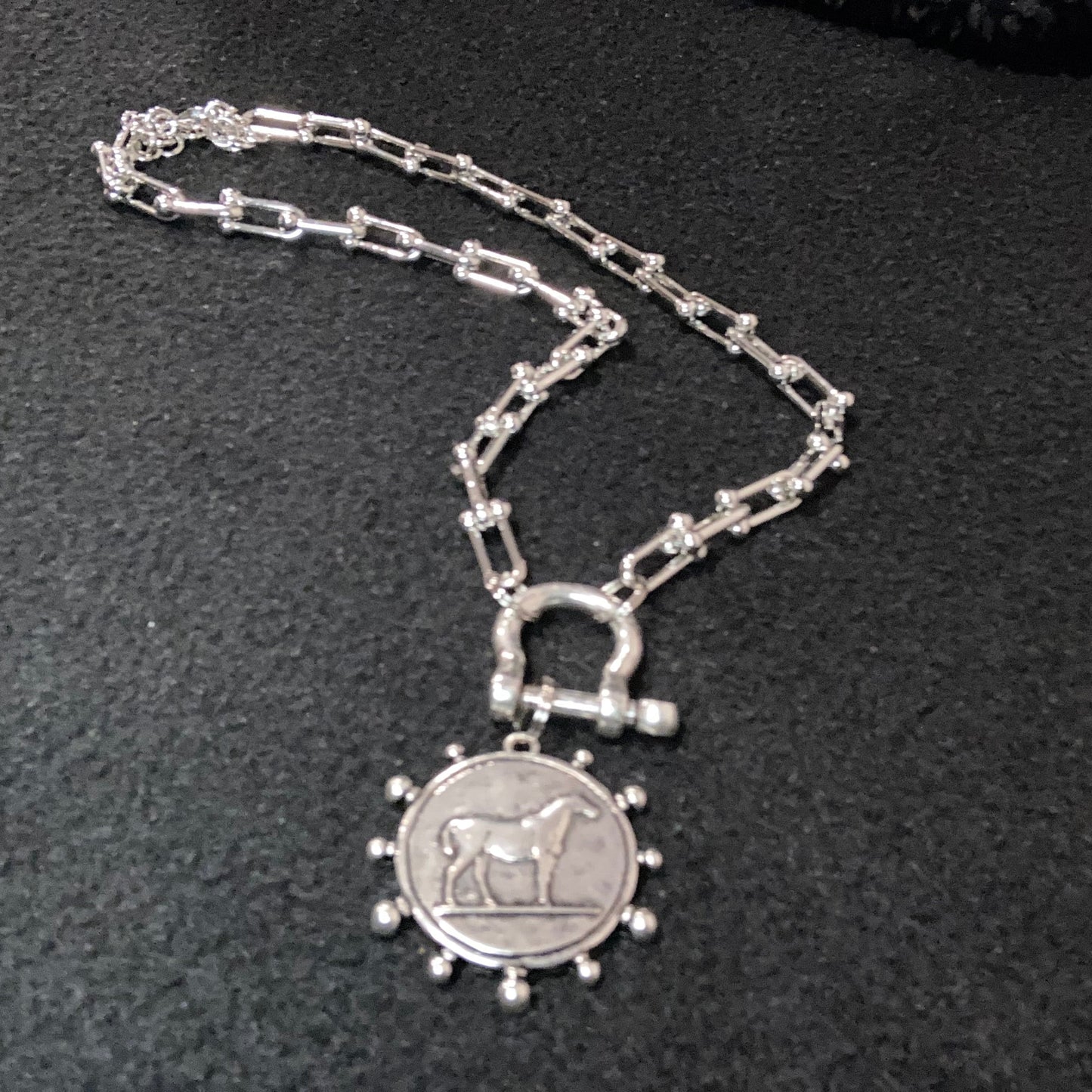 Silverplated paperclip necklace with horse charm on a dark surface