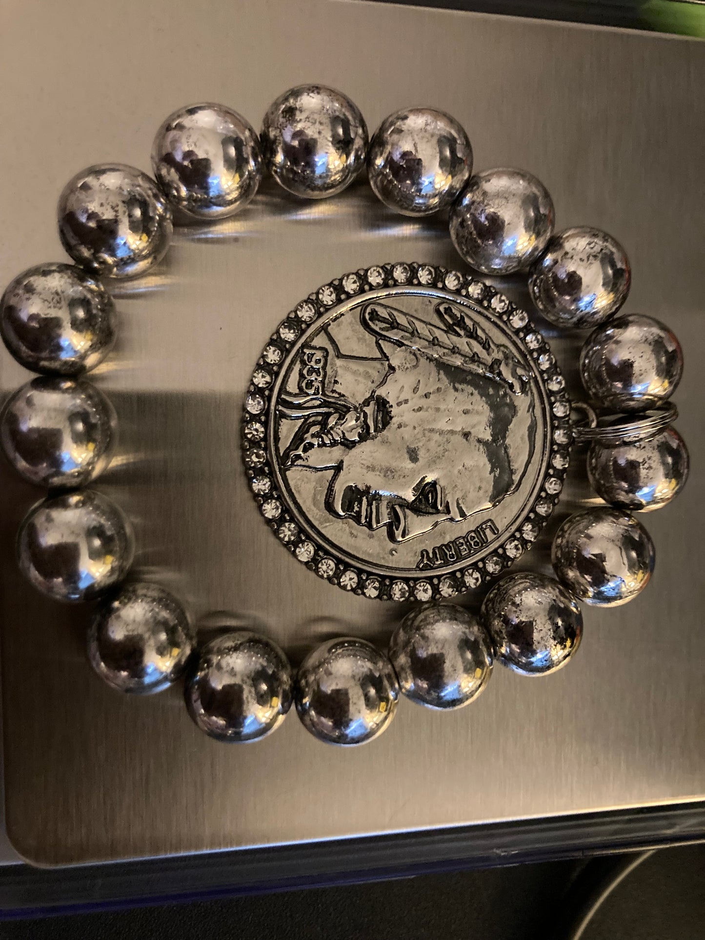 Silver beaded bracelet with a central emblem on a reflective surface