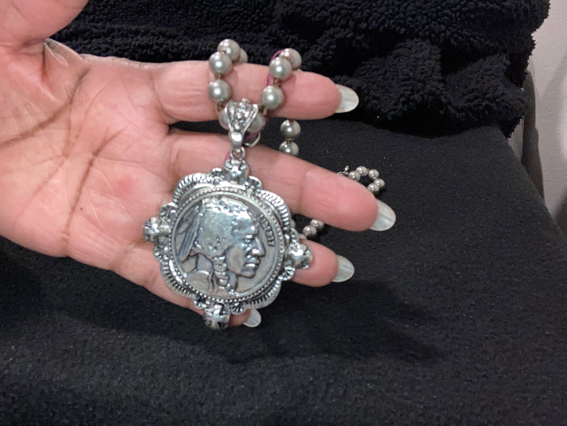 Silver Plated Indian head in a hand against a black background