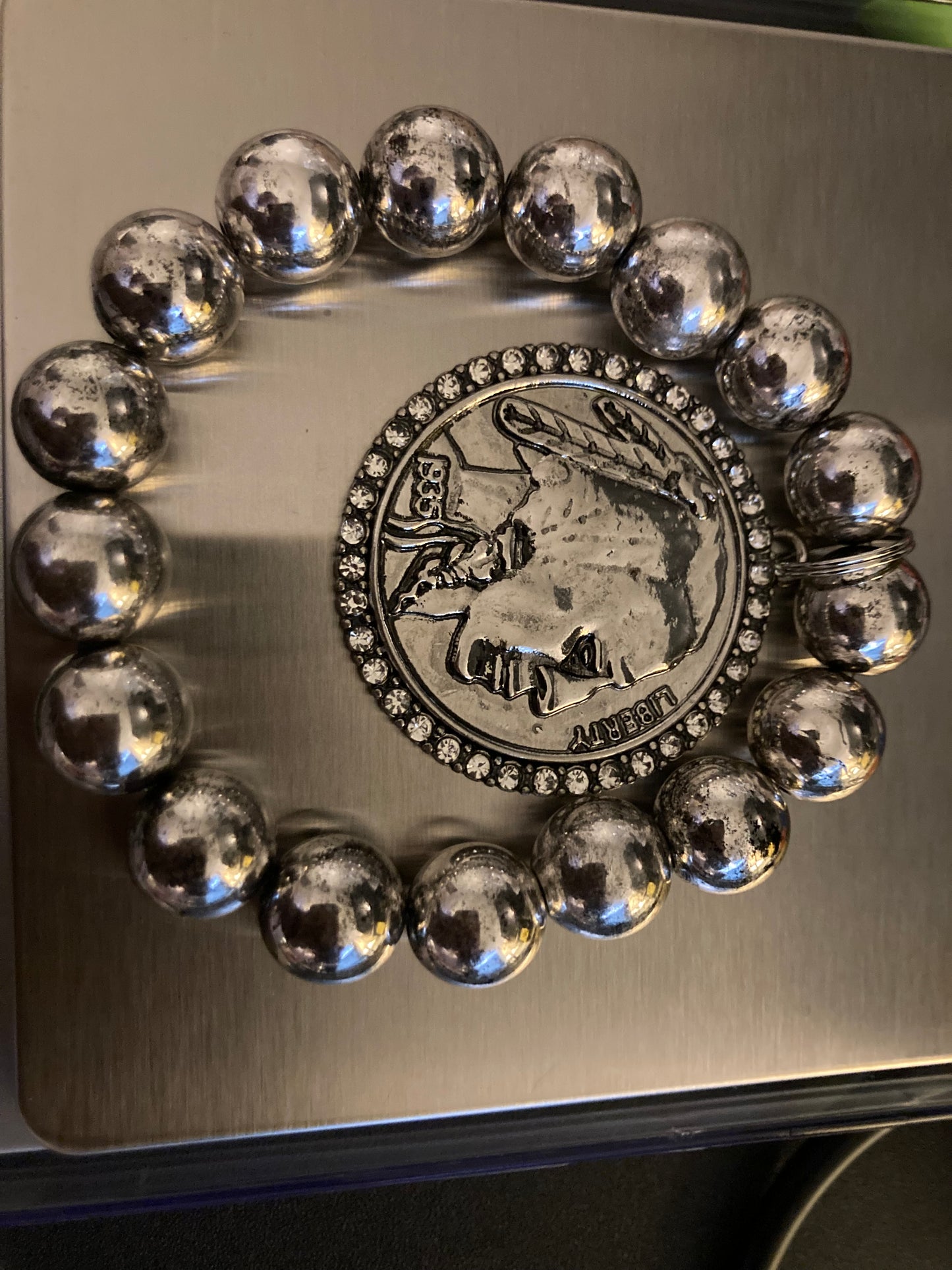 Silver beaded bracelet with a coin charm featuring a face design on a metallic surface.
