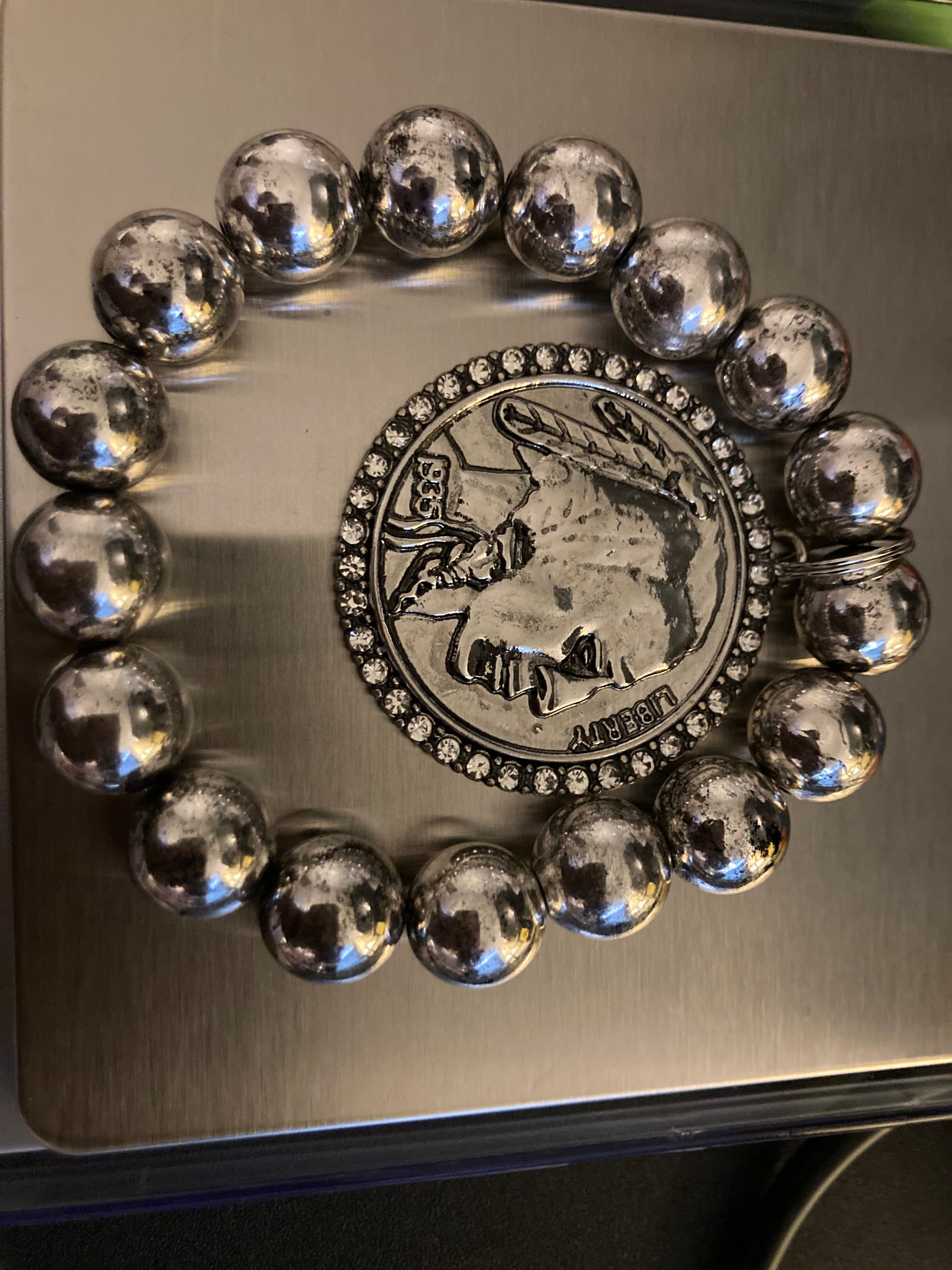 Silver beaded bracelet with a coin charm featuring a face design on a metallic surface.