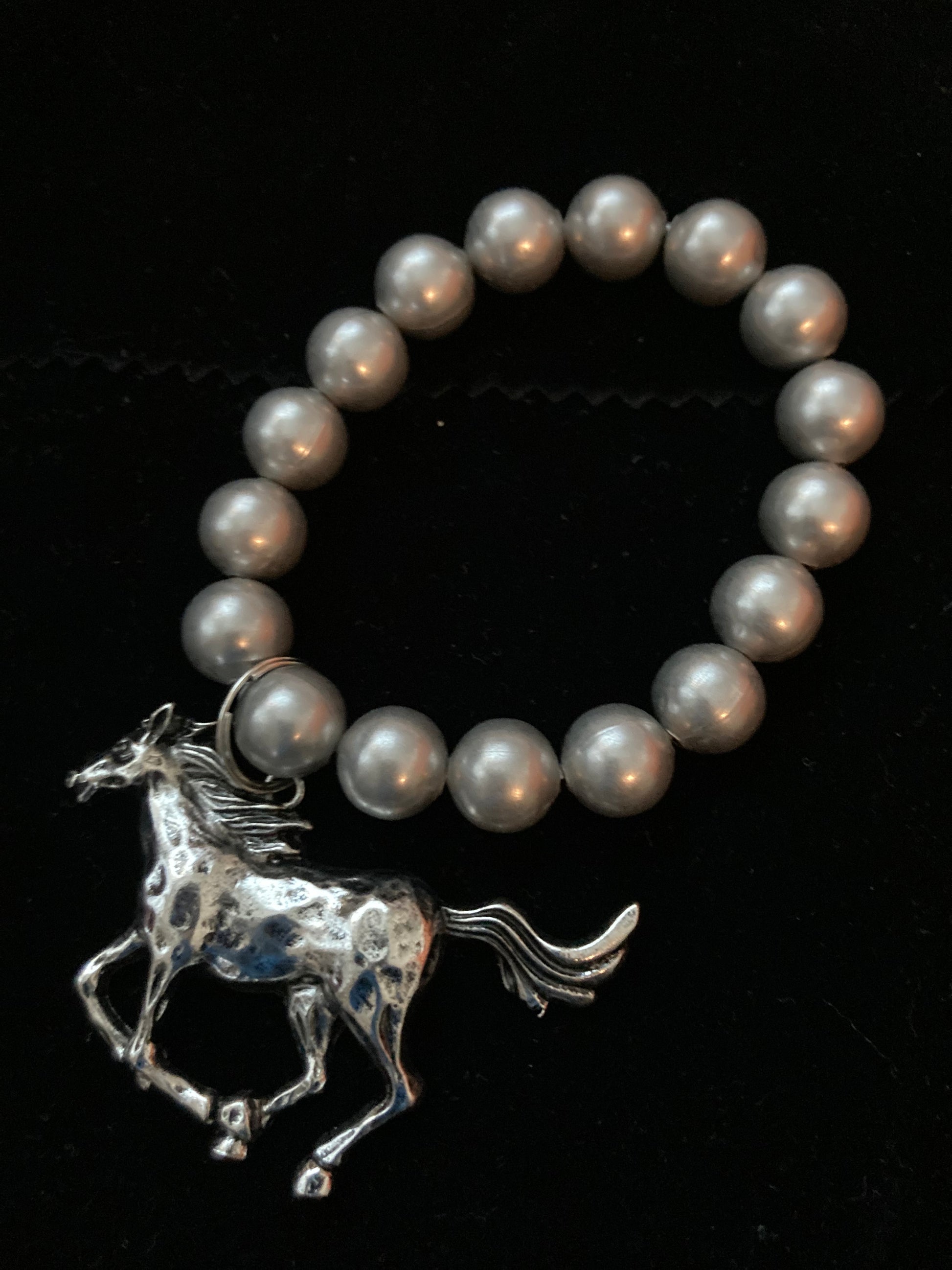 Pearl bracelet with a silver horse charm on a black background