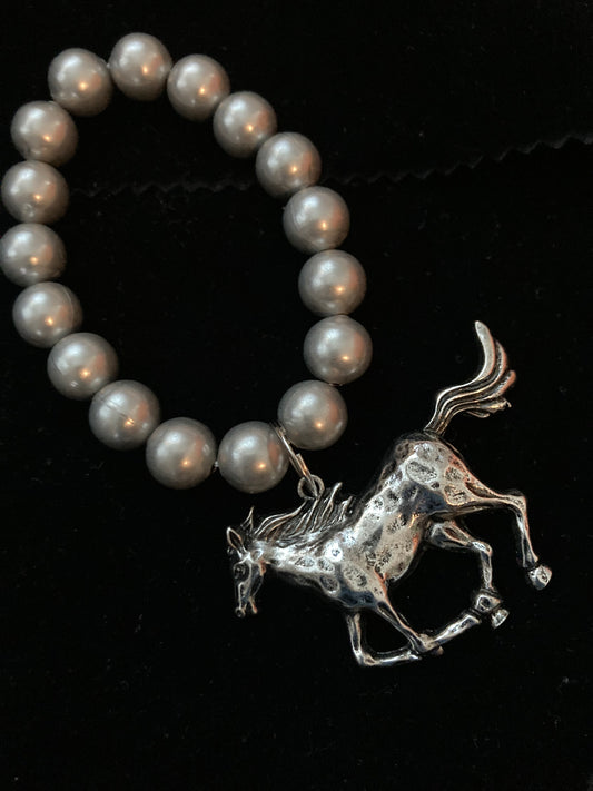 Pearl bracelet with a silver horse charm on a black background
