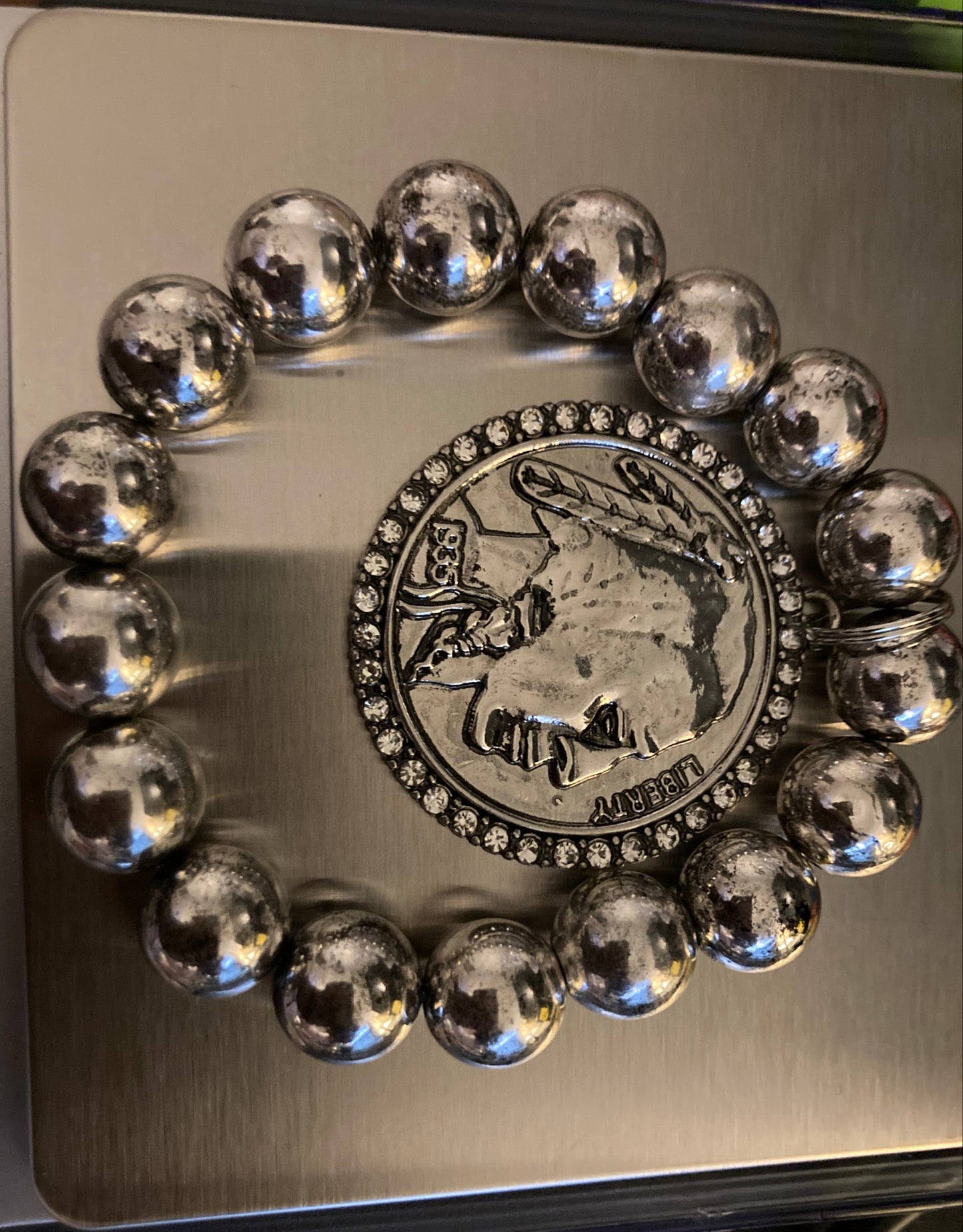 Silver beaded bracelet with a coin charm on a metallic surface