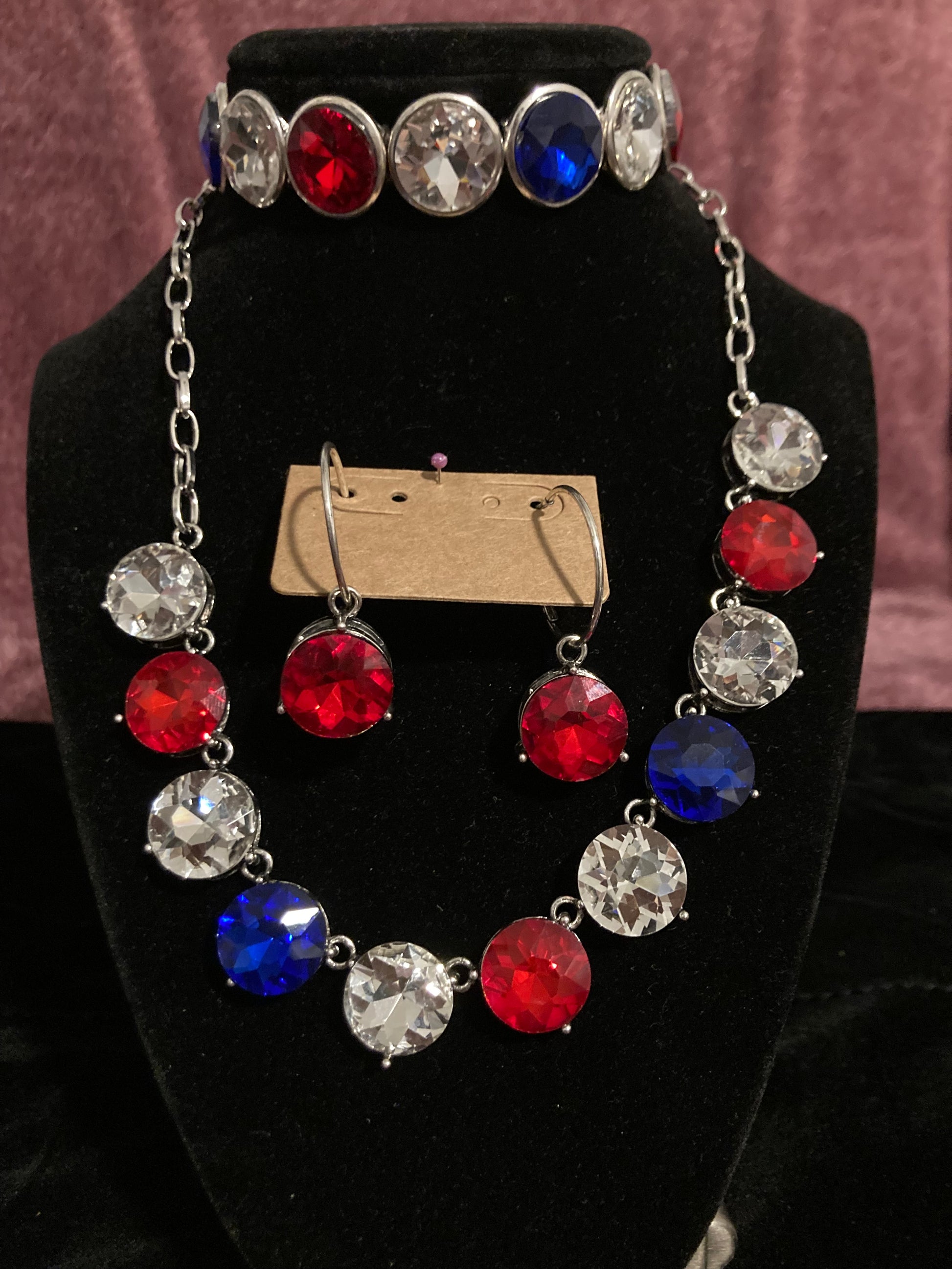 Necklace with red, blue, White cleargemstones on a black stand.