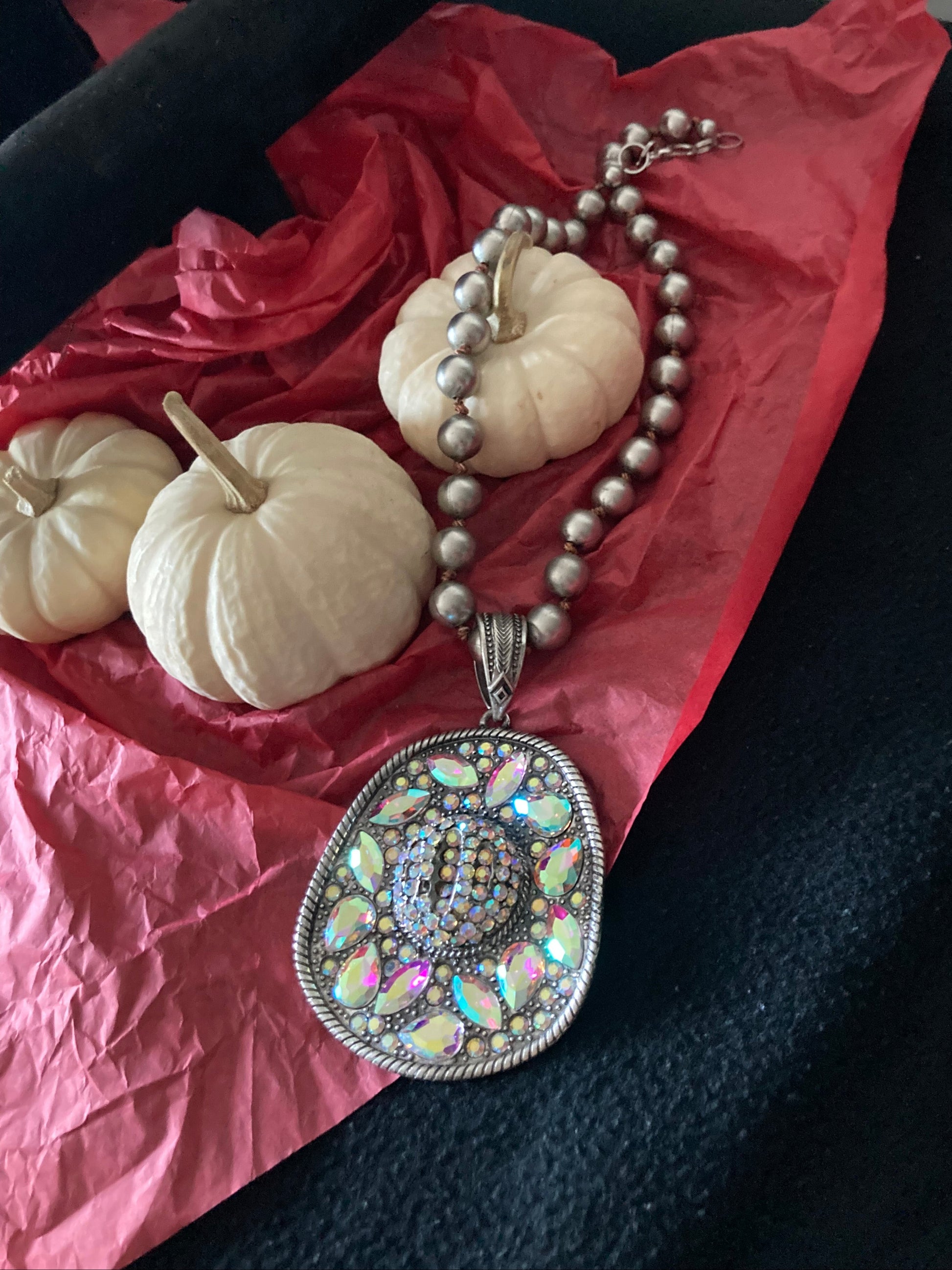 Decorative items including a Gemstone Pendant Hat necklace, decorative pumpkins, and a red fabric.
