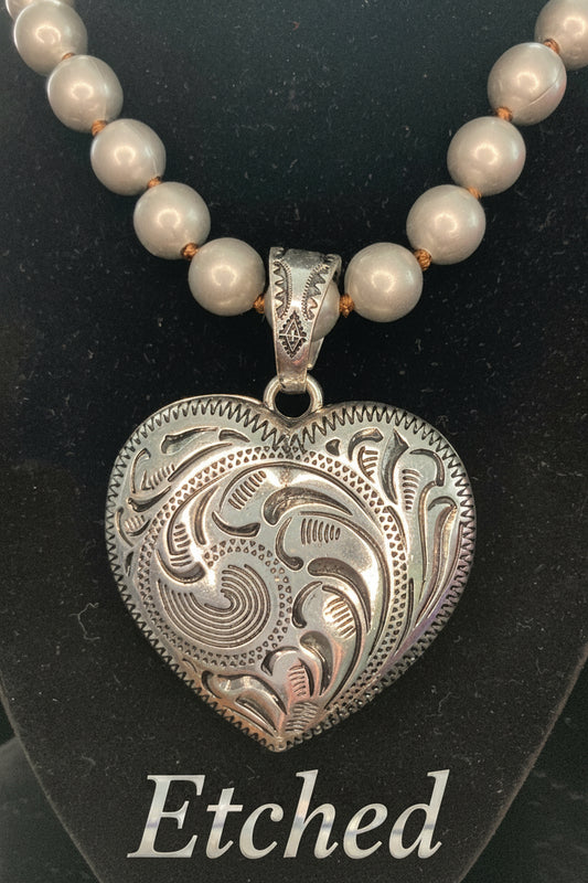 Silver heart-shaped pendant on a necklace with Silver beads against a black background