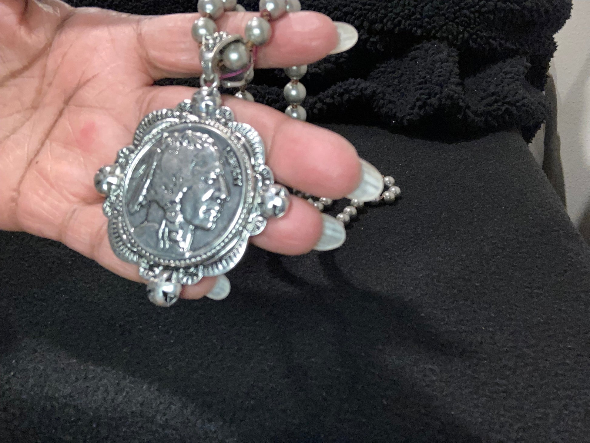 Hand holding a silver-plated pendant of Indian head against a dark background