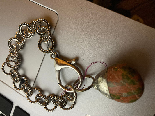 Brass chain with a charm clamp and a round stone on a light gray surface