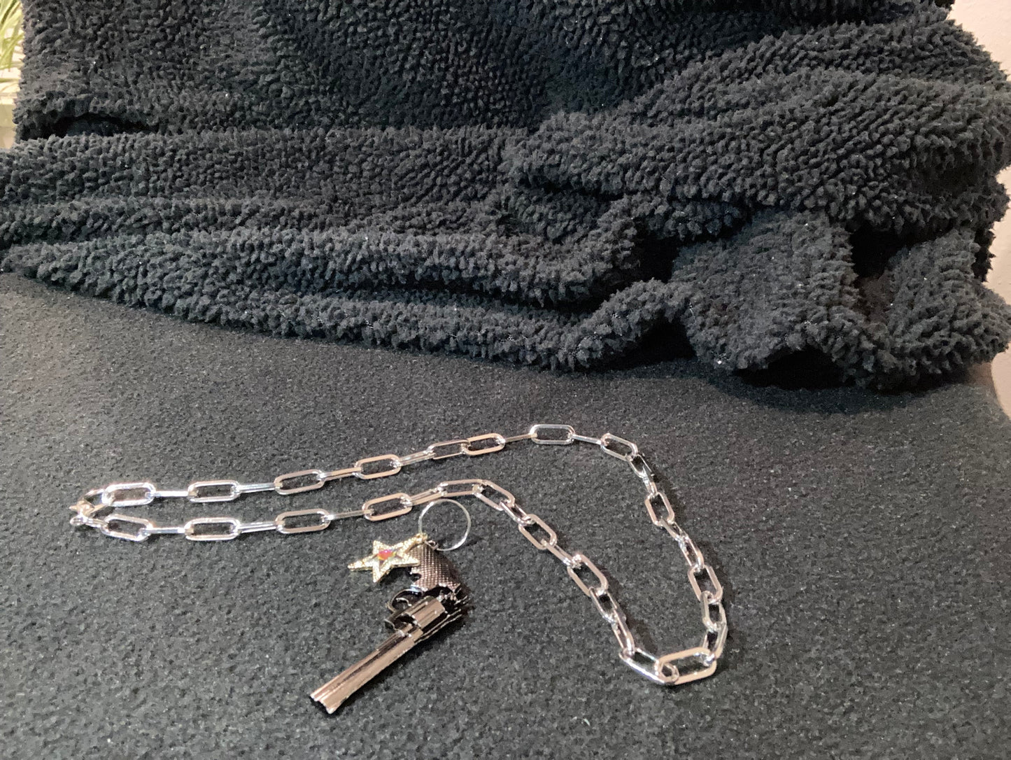 Close-up of Silver-Plated a chain with a gun and star charm on a textured gray surface