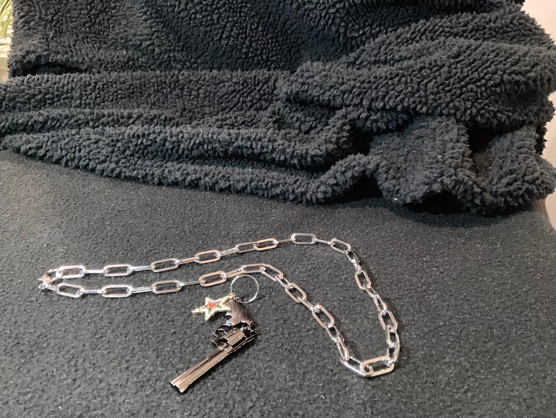 Close-up of Silver-Plated a chain with a gun and star charm on a textured gray surface