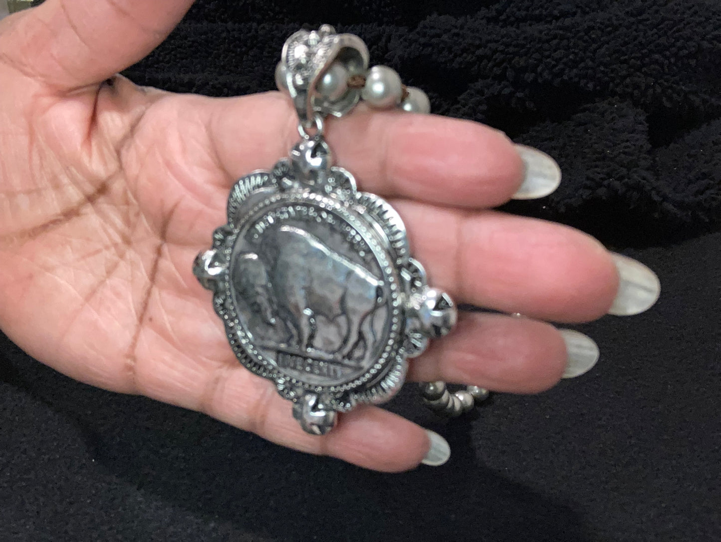 Silver plated bison pendant necklace held in a hand against a dark background