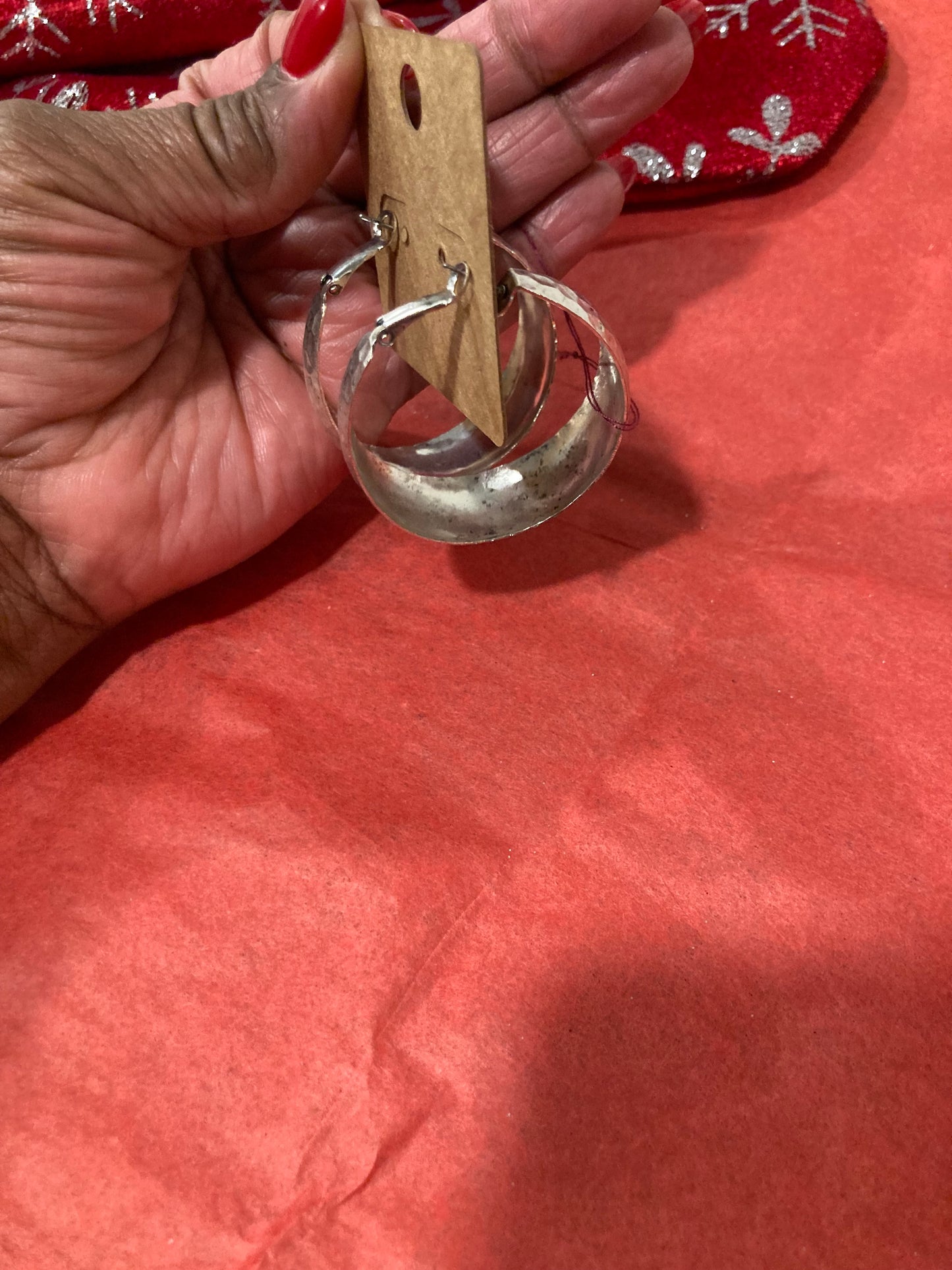 Hand holding a Silver-Plated Hoop Earrings against a red fabric background