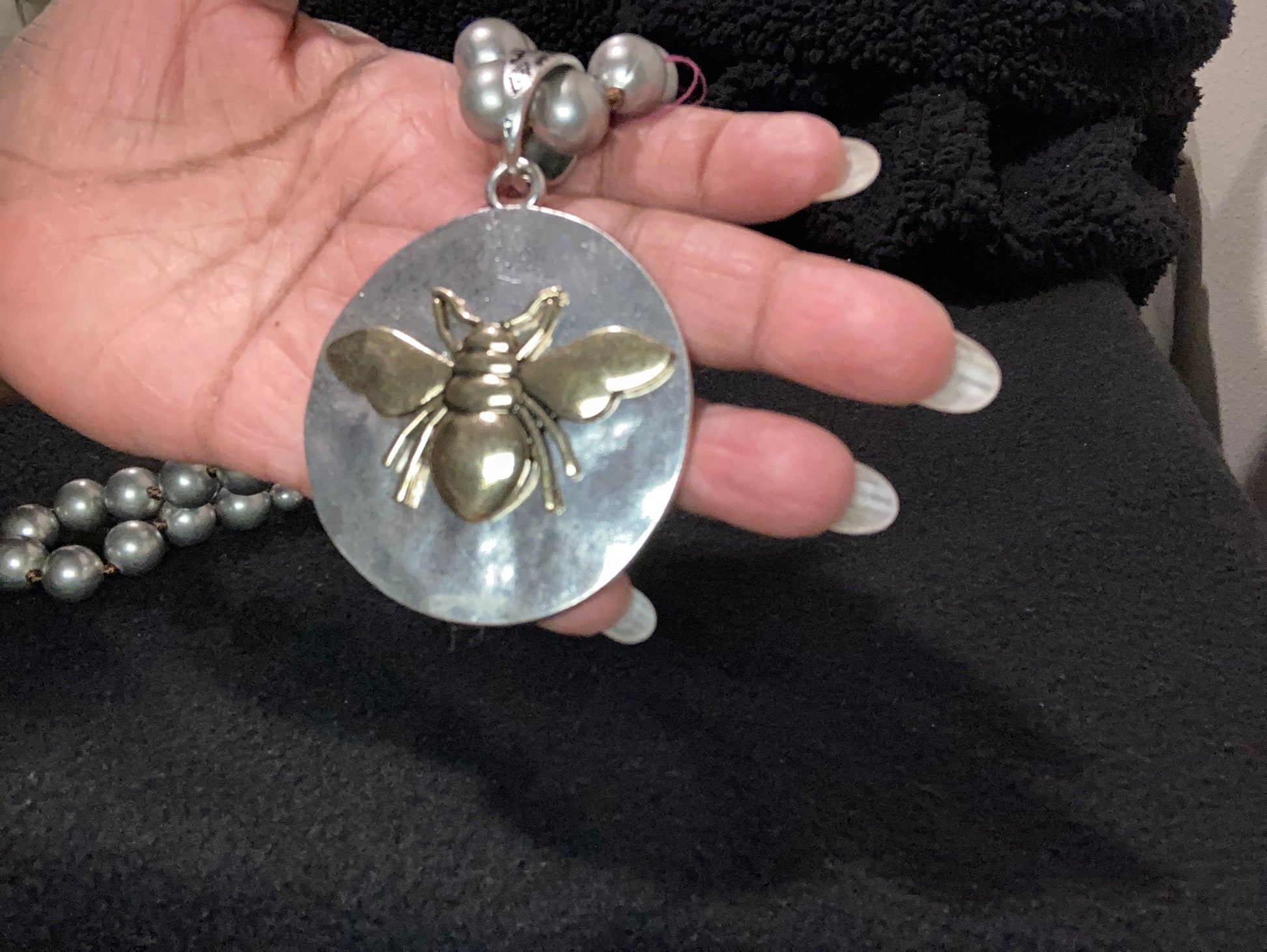 Hand holding a silver-plated pendant with a gold bee design against a black background