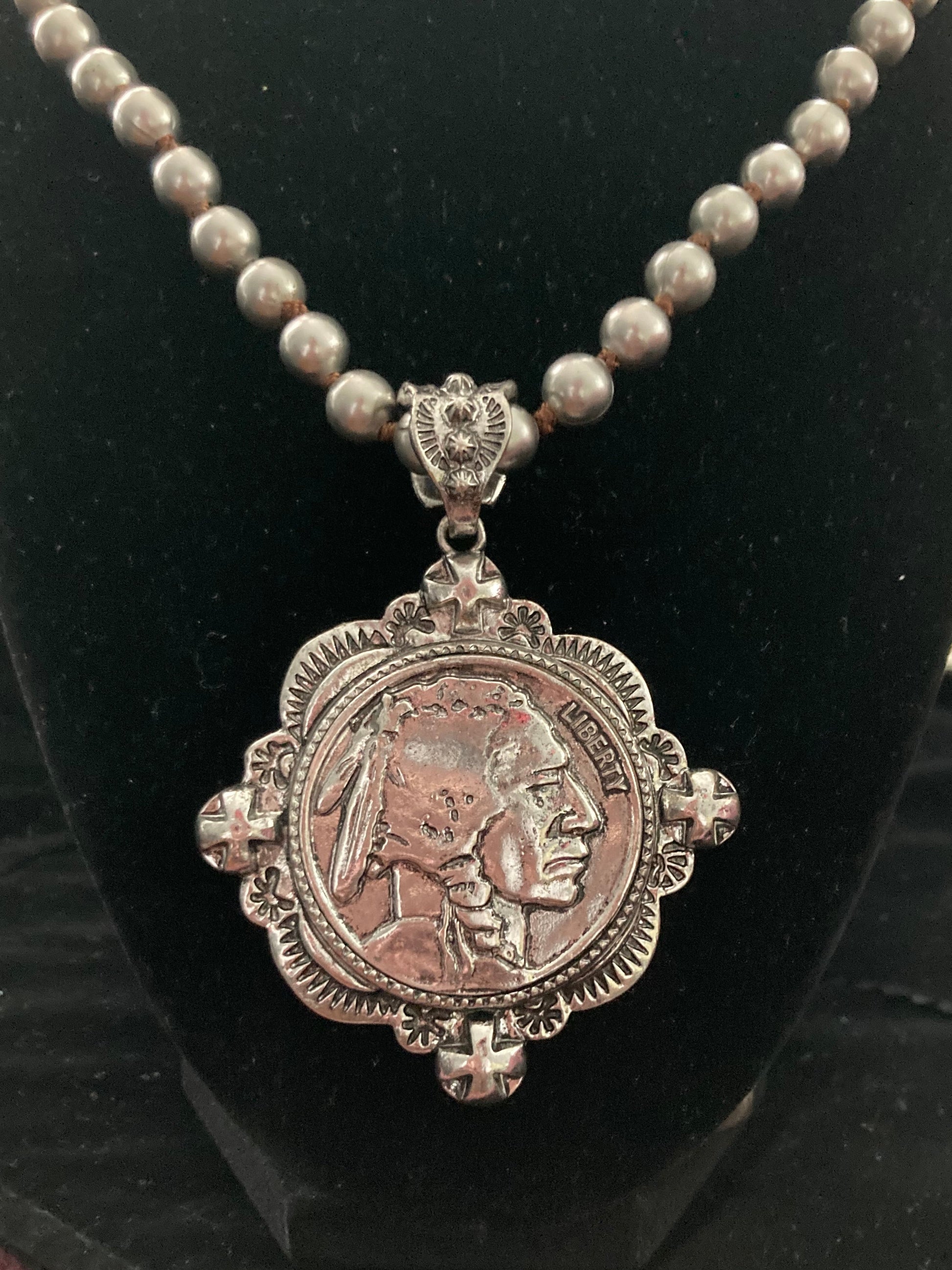 Silver necklace with a pendant featuring an Indian face on a black stand.