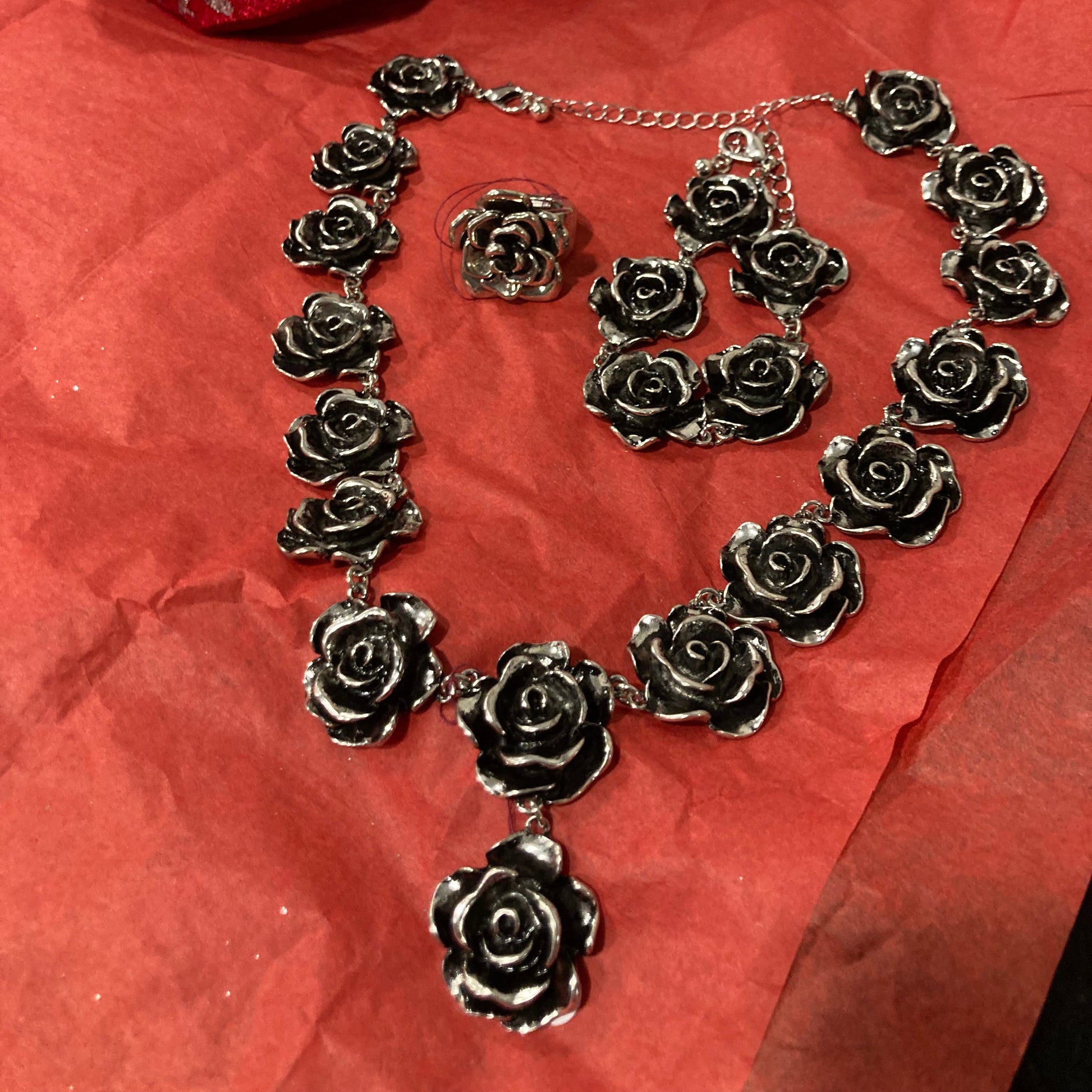 Silver rose necklace and on a red Bracelet and ring on surface with a red fabric background.