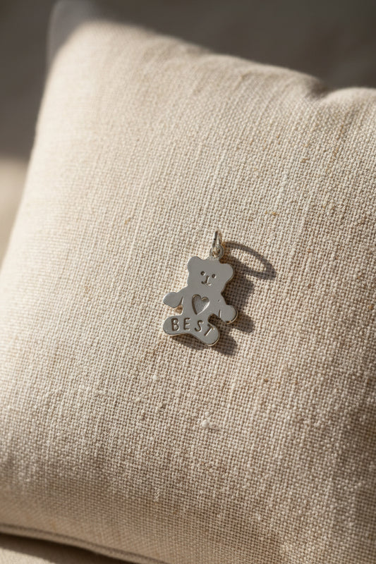 Silver teddy bear charm with 'I love you best' text on a beige background