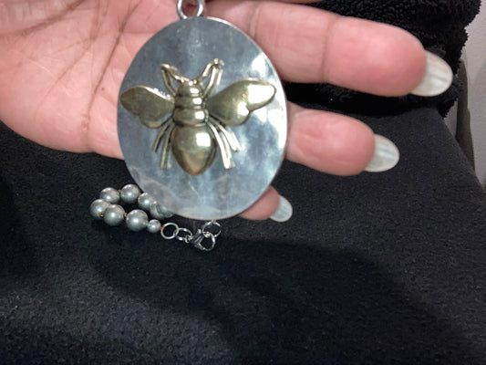 Silver Plated pendant with a Bee design held in a hand against a black background