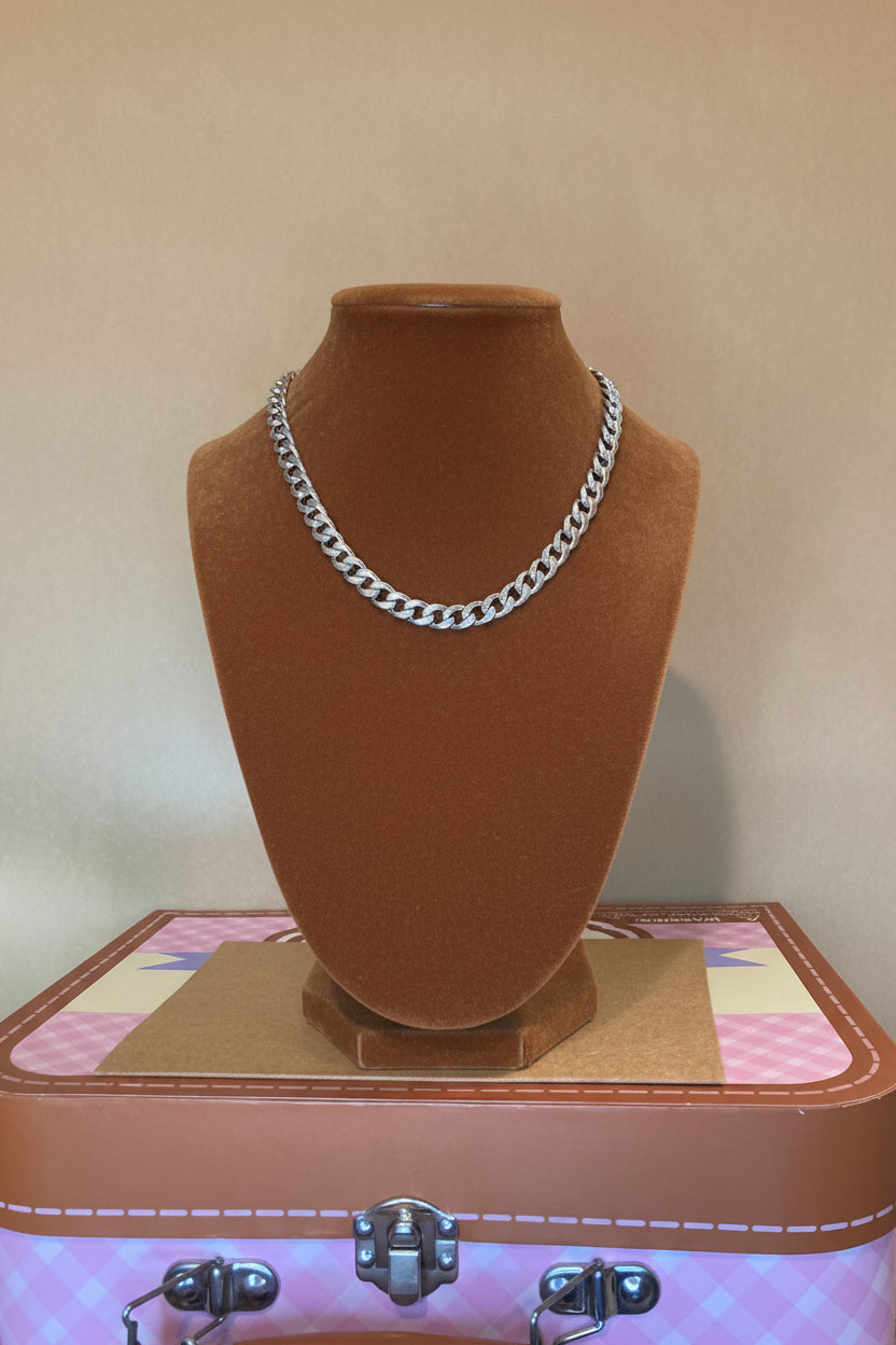 Black form with Cuban Link Bracelet strap on a surface  a top pink and Carmel suitcase.