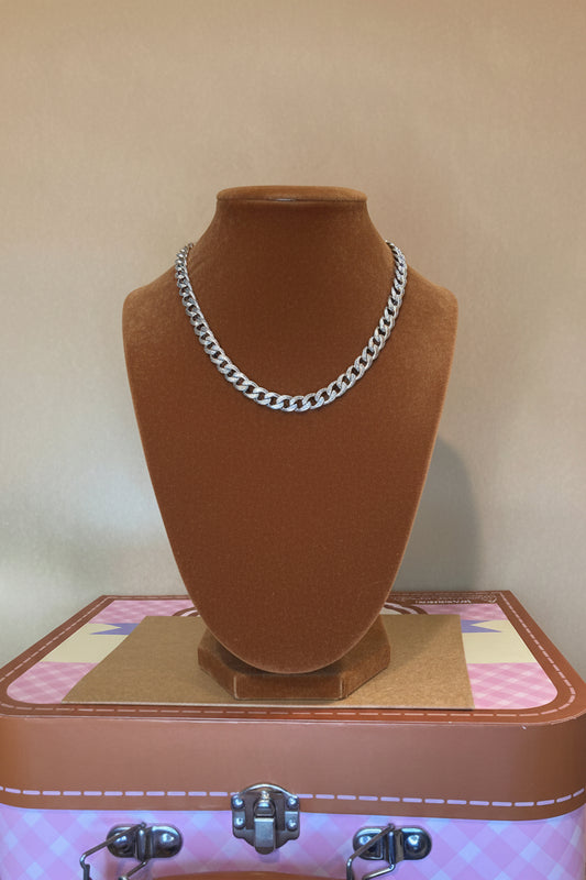 Black form with Cuban Link Bracelet strap on a surface  a top pink and Carmel suitcase.