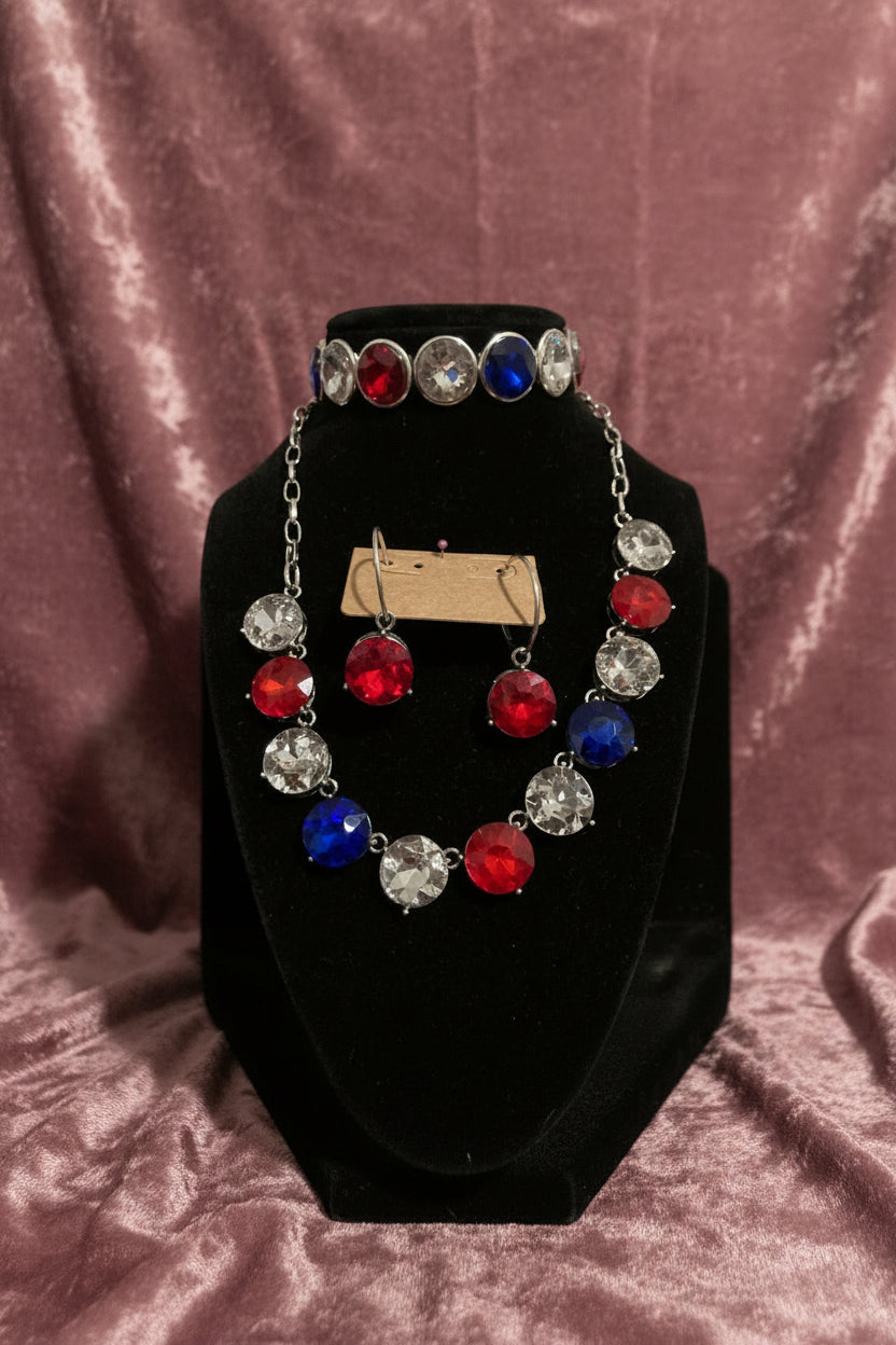 Necklace Earrings and Bracelet with red, blue, and clear gemstones on a black stand.