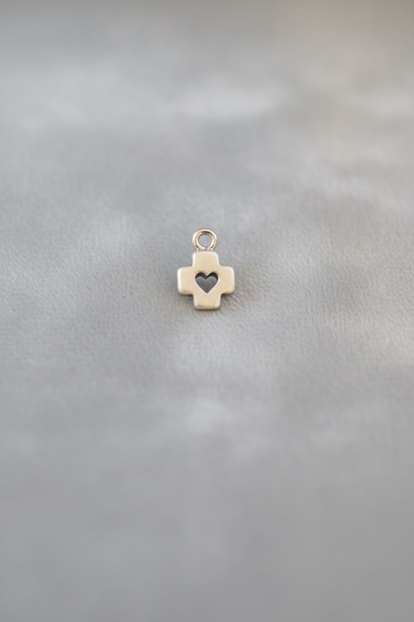Small gold cross charm with a heart on a black background