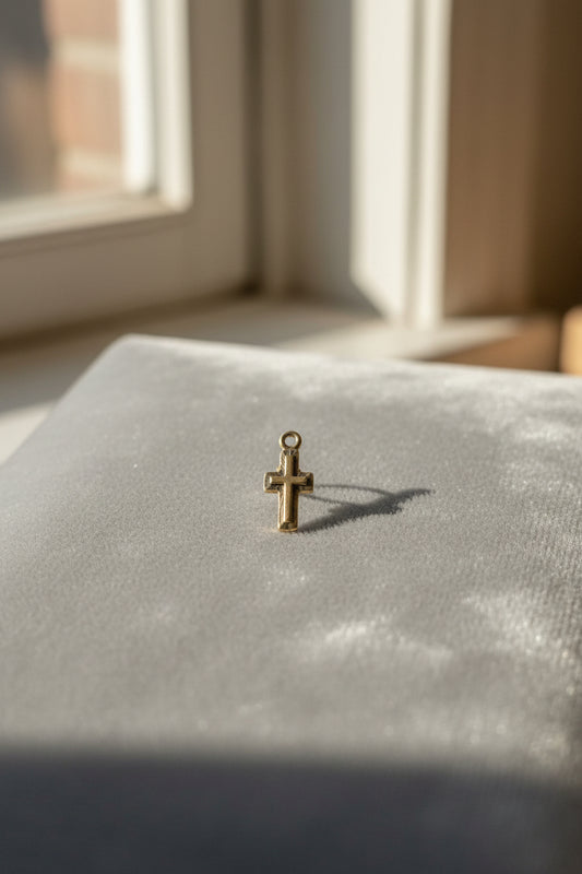 Small Silver cross pendant/Charm on a textured surface with a window in the background